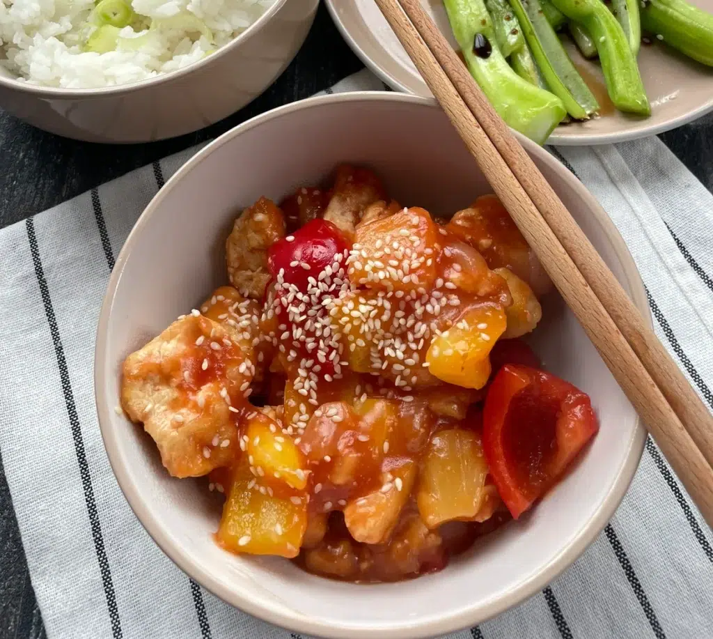 Tofu chunks with red bell peppers and onions cooked in a sweet and sour sauce garnished with sesame seeds. Served with white rice and stir fried chinese leaf vegetables