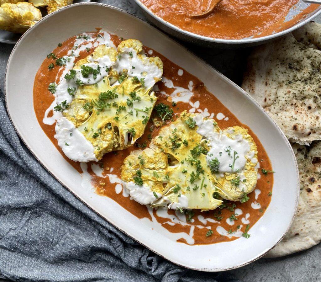 Roasted cauliflower steaks served on a bed of butter curry sauce topped with a cashew cream drizzle and fresh parsley sprinkle