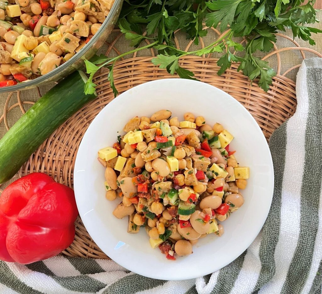 A white bowl of bean salad with fresh veggies around