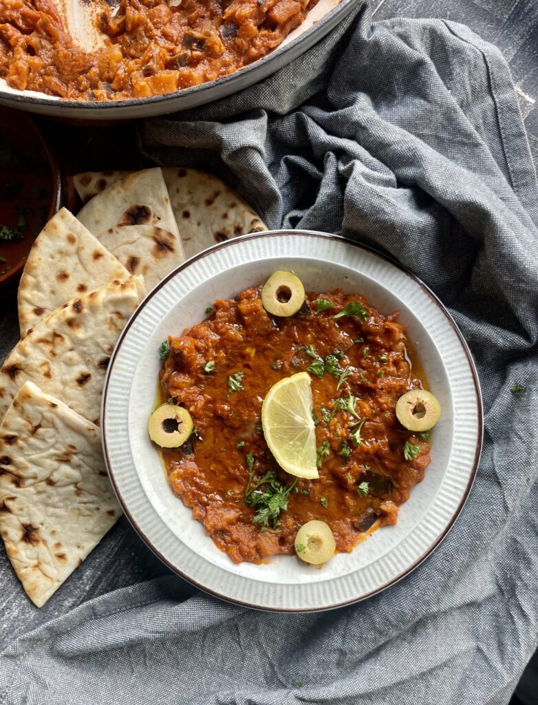Eggplant and tomato dip with Moroccan spices. topped with a drizzle of olive oil, lemon slice and sliced green olives served with flatbreads