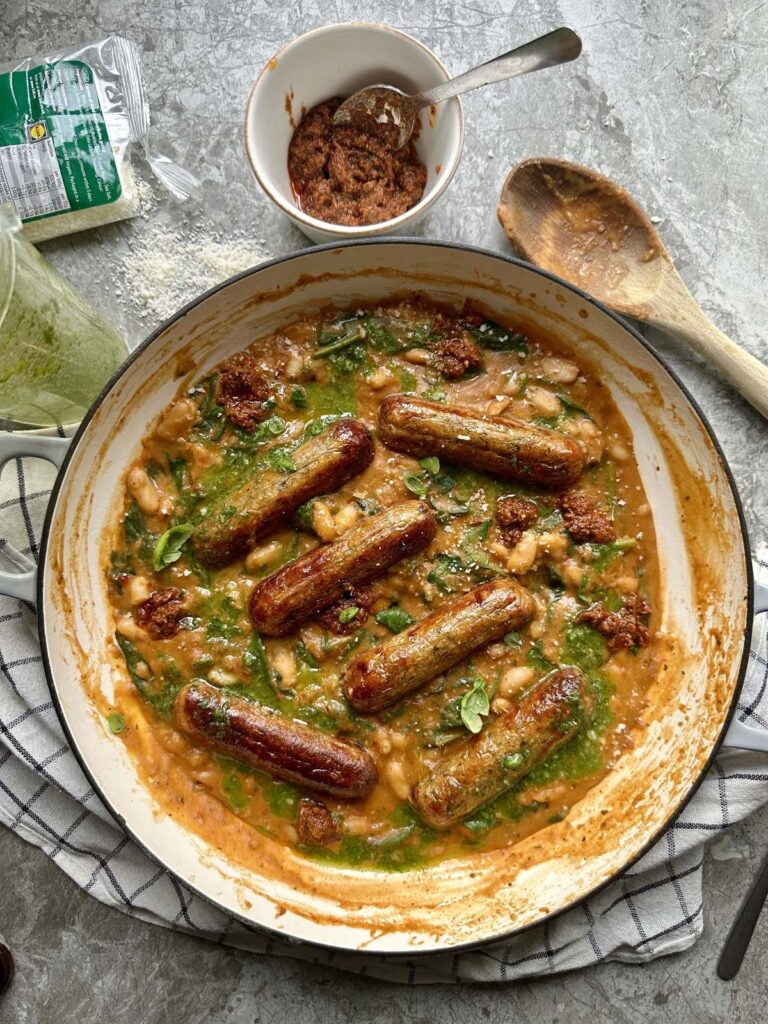 Creamy red pesto beans topped with sausages and fresh basil oil