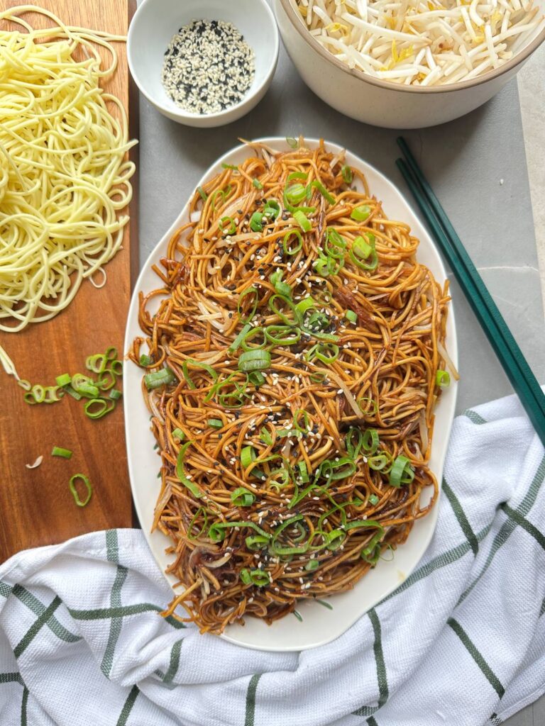 Plain chow mein on a serving platter topped with sesame seeds and spring onion