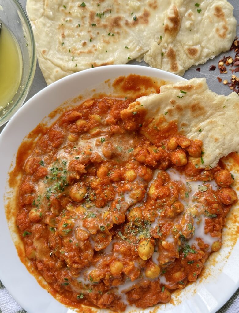 Close up of the chickpea curry topped with coconut milk and a piece of garlic naan in the bowl to scoop it up