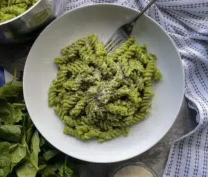 Fusili pasta cooked in a creamy spinach pesto sauce topped with vegan parmesan