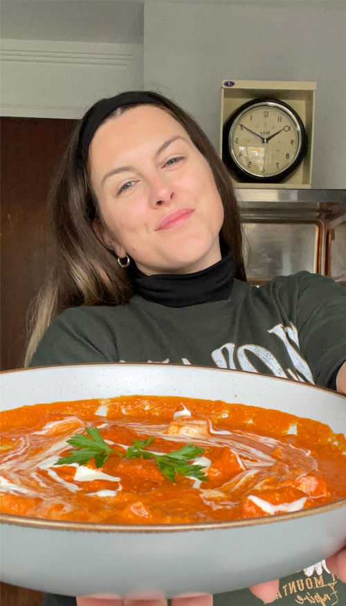 Abbie, the website owner, smiling presenting a bowl of bright orange tikka masala curry {{brizy_dc_image_alt imageSrc=