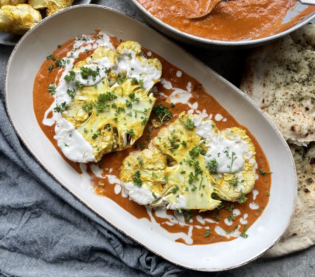 Roasted cauliflower steaks served on a bed of butter curry sauce topped with a cashew cream drizzle and fresh parsley sprinkle