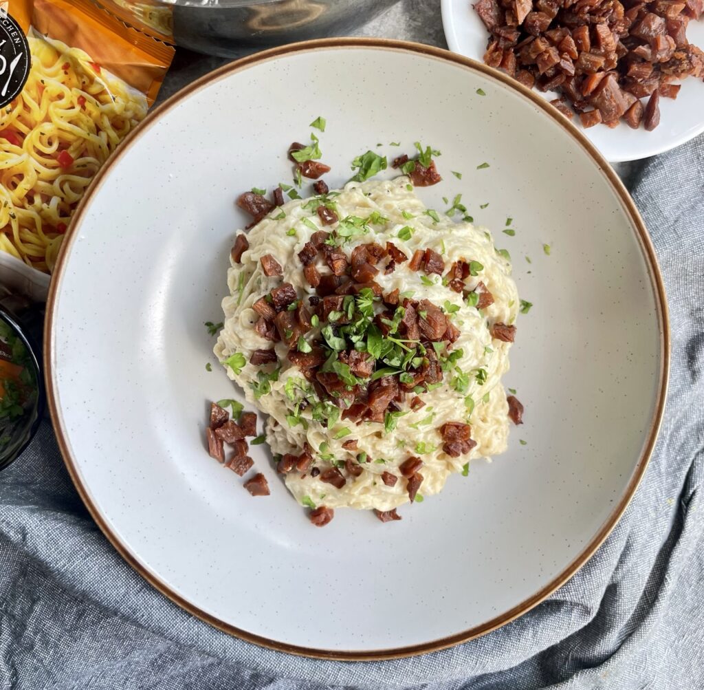 Instant noodles cooked in a creamy smokey carbonara sauce topped with crispy vegan bacon lardons and fresh parsely