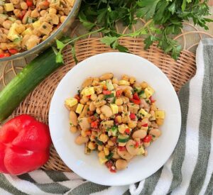 A white bowl of bean salad with fresh veggies around