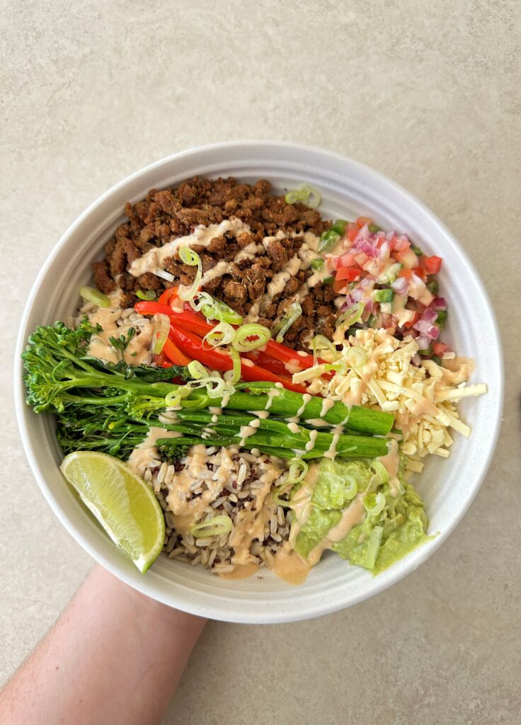 A burrito bowl containing Spiced vegan mince with rice, pico de gallo, avocado, broccolini and chipotle mayo