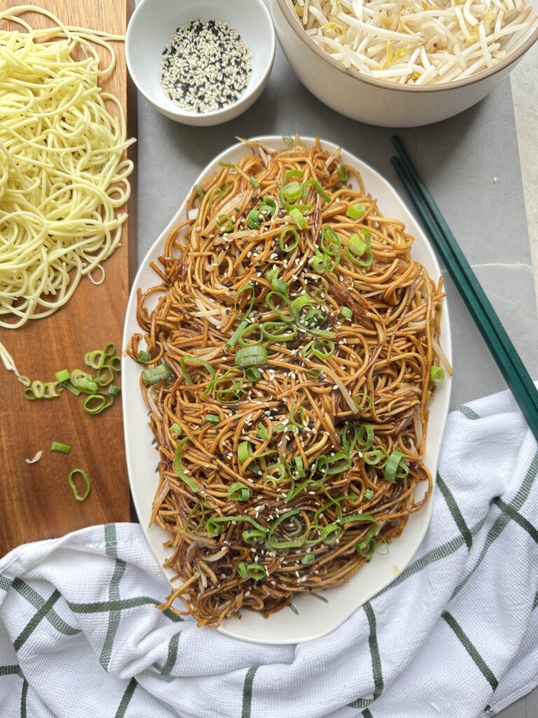 Plain chow mein on a serving platter topped with sesame seeds and spring onion