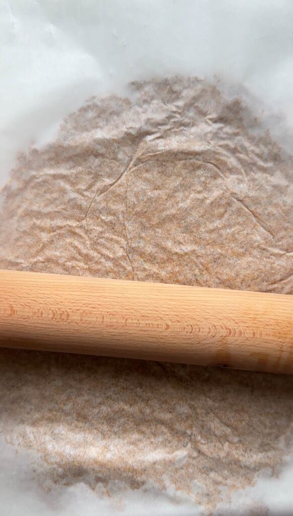 sheet of baking paper on top of the doner mix and being rolled out with rolling pin