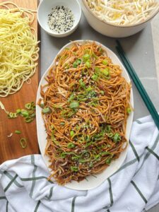 Plain chow mein on a serving platter topped with sesame seeds and spring onion
